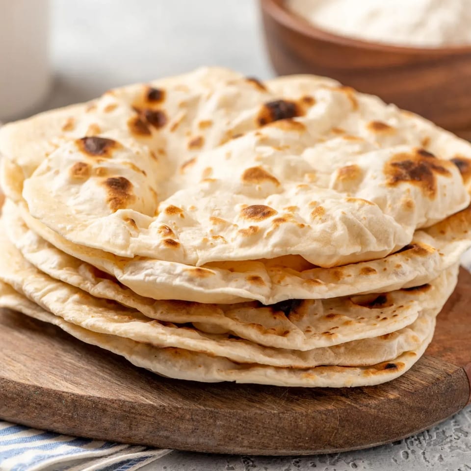 Stack of warm, golden-brown flatbreads on a wooden board with a blue striped towel.