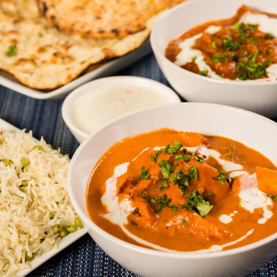 Indian butter chicken, rice, naan bread, and raita on a blue placemat.