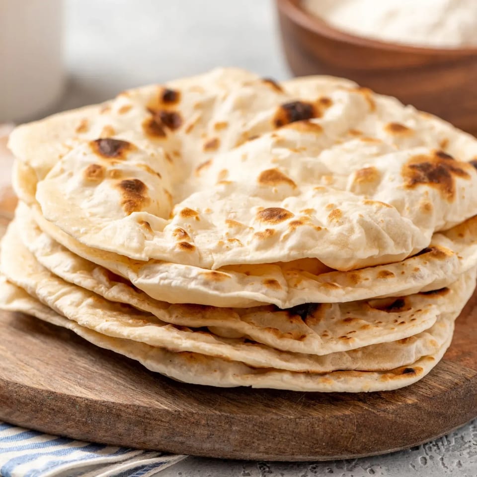 Stack of freshly baked flatbreads with golden-brown spots on a wooden board.