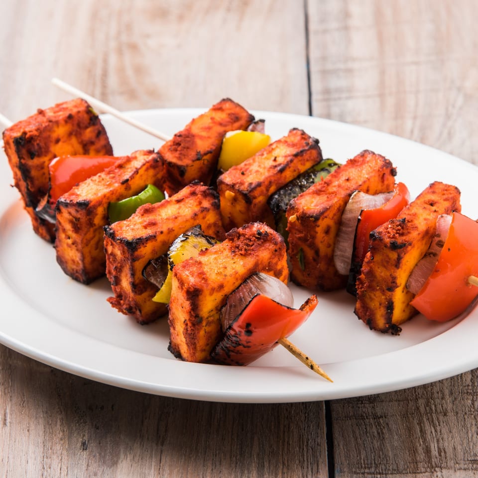 Grilled paneer tikka skewers with red and green bell peppers and onions on a white plate.