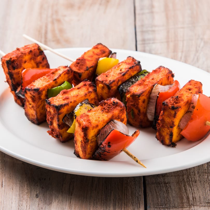 Grilled paneer tikka skewers with red and green bell peppers and onions on a white plate.