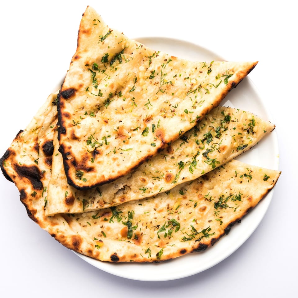 Golden-brown garlic naan bread, garnished with fresh cilantro and spices, on a white plate.