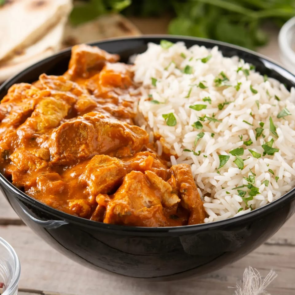 A black bowl filled with chicken tikka masala and white rice, garnished with parsley.